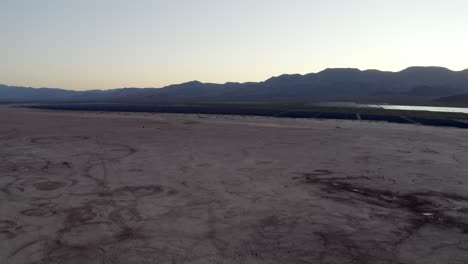 Lecho-Seco-Del-Lago-Nevada-Al-Atardecer-La-Inclinación-Del-Carro-Aéreo-Hacia-Arriba-Revela-Montañas-Y-Un-Atardecer-Brumoso