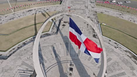Aerial-top-down-shot-of-swaying-flag-on-famous-memorial-at-Plaza-de-la-Bandera,-Dominican-Republic