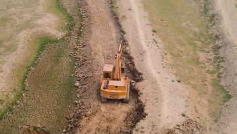 Caterpillar-bulldozer-orbiting-aerial-view-digging-dirt-trench-on-construction-site-with-scoop