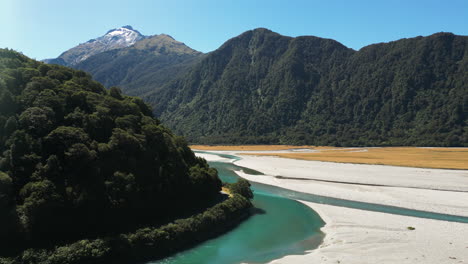 Toma-Aérea-De-Drones-De-Un-Río-Angosto-Verde-Claro-Rodeado-Por-Una-Cordillera-Cubierta-De-Vegetación-Verde-En-Piscinas-Azules,-Nueva-Zelanda
