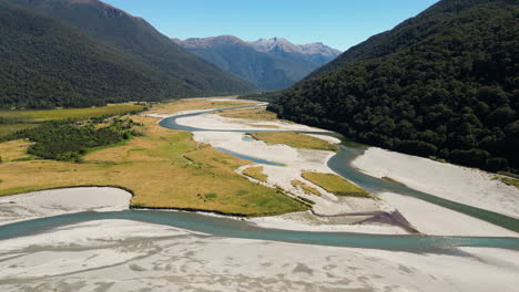aerial-scenic-view-of-stunning-New-Zealand-NZ-landscape-with-river-stream-clean-pristine-water-leading-to-mountains-during-clear-sky-sunny-weather