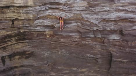 Mädchen-In-Einem-Gelben-Bikini-Springt-Von-Der-Spuckenden-Höhlenklippe-Ins-Blaue-Wasser-In-Honolulu,-Hawaii-–-Rückzug-Aus-Der-Luft