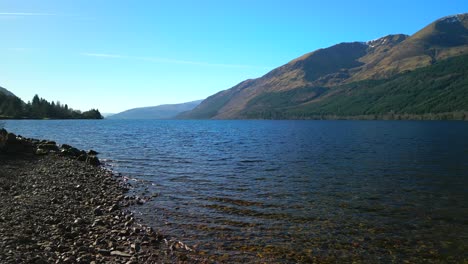 Traveller-sat-on-rock-with-flyover-onto-lake-water-at-Loch-Lochy-Scottish-Highlands