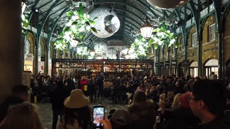 Walking-around-Covent-Garden-in-London-in-December-2022-and-showing-live-street-performers-and-crowds-and-showing-how-busy-the-location-is-with-tourists-in-the-evening-during-this-festive-period