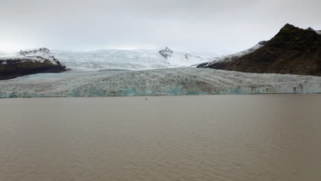 Luftaufnahme:-Flug-Auf-Ein-Kleines-Boot-Mit-Touristen-In-Der-Nähe-Des-Fjallsarlon-Gletschers-In-Südisland-An-Einem-Bewölkten-Tag