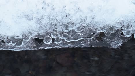 Close-up-shot-of-flowing-river-water-under-ice-covernd-with-snow