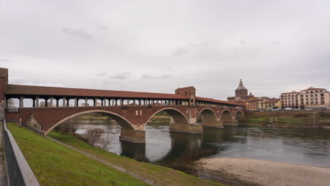 Ponte-Coperto-is-a-bridge-over-the-Ticino-river-in-Pavia,-Pavia-Cathedral-background,-time-lapse-at-cloudy-day