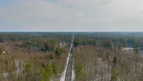 Backward-drone-view-flight,-tracking-a-car-that-is-driving-on-a-road-of-a-wintry-forest