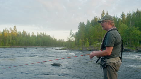Fly-fisherman-fishing-in-a-river-with-rapids-in-the-background-casting-with-his-fly-rod-on-a-summer-night