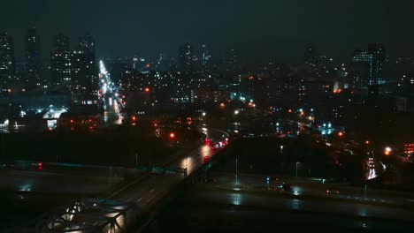 Drone-flying-over-rooftop,-Manhattan-skyline-at-night,-highway-river