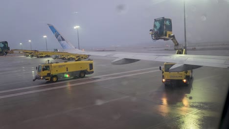 Frontier-aircraft-wing,-N344FR,-undergoes-deicing-following-freezing-rainstorm-at-DTW-viewed-from-inside-aircraft-ending-with-deicing-fluid-splashing-on-viewing-window