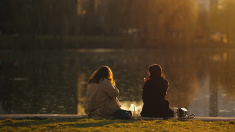 Two-friends-having-lunch-together-in-shores-of-a-lake-in-park-with-amazing-sunset-light