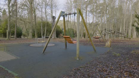Children's-empty-playground-single-orange-swing-chair-rocking-alone-in-woodland-autumn-forest