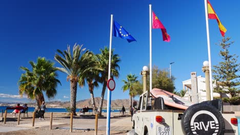 Flags-and-old-Landrover-in-La-Azohía-beach,-Murcia,-Spain