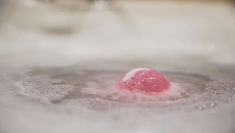 Close-up-of-pink-bath-bomb-dissolving-by-surface-in-bubbly-bathtub