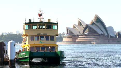 Passengers-embark-a-Sydney-ferry-in-front-of-the-Sydney-opera-house,-Australia