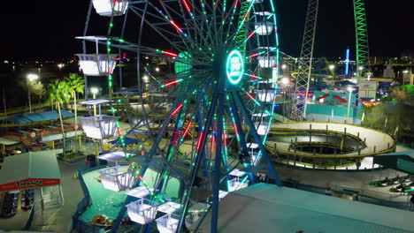Aerial-view-in-front-of-a-night-lit-ferris-wheel-at-a-theme-park-in-Orlando,-Florida---tracking,-tilt,-drone-shot