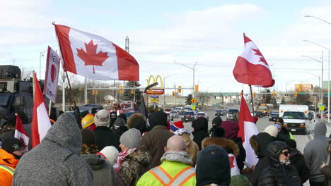 Protesters-with-flags-stand-on-blocked-road-in-front-of-armed-soldiers-and-police,-Freedom-convoy