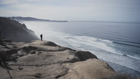 Lonely-person-admires-ocean-waves-from-tall-cliff,-handheld-view