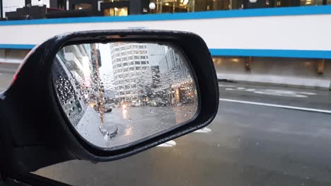 Inner-city-traffic-in-capital-city-of-Wellington-in-New-Zealand-Aotearoa,-vehicle-lights-and-rain-drops-in-car-wing-mirror-view