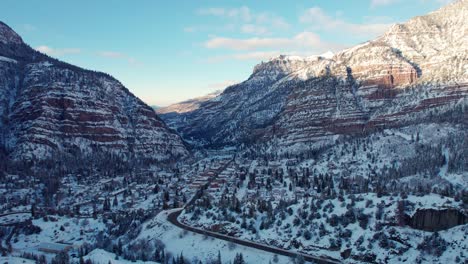 Sunrise-drone-aerial-flyover-of-Ouray,-Colorado-in-the-winter-covered-in-snow