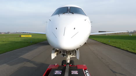 Point-of-view,-Embraer-ERJ135-towed-by-tow-truck,-Antwerp-Airport,-spring