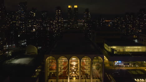 Aerial-view-in-front-of-the-illuminated-Lincoln-Center-for-the-Performing-Arts,-night-in-NY,-USA---ascending,-drone-shot