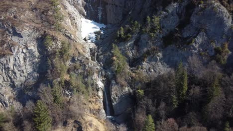 Aerial-approach-of-a-mountains-waterfall-with-snow-on-top