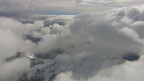 Luftaufnahme-Durch-Dichte-Wolken-Mit-Flecken,-Die-Die-Verschneite-Landschaft-Darunter-Freigeben