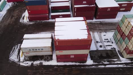 Metal-shipping-containers-covered-in-white-snow,-aerial-drone-view