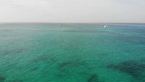 Dolly-Aéreo-Sobre-Las-Hermosas-Aguas-Del-Océano-Azul-Turquesa-Hacia-Dos-Catamaranes-Que-Navegan-En-Sal-Cabo-Verde
