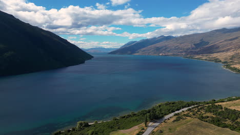 Blauer-See-Zwischen-Bergen-Mit-Landstraße-In-Neuseeland,-Luftaufnahme