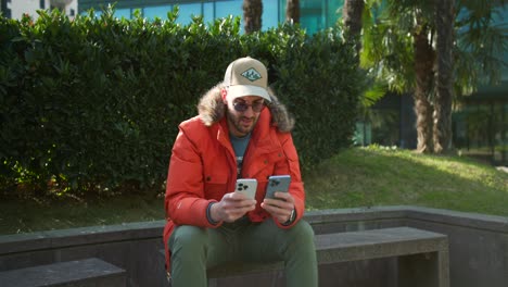 Man-in-an-orange-jacket-working-on-two-new-smartphones