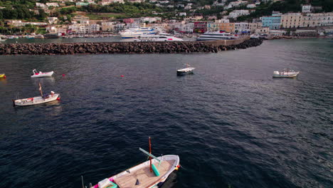 A-cinematic-wide-drone-shot-tilting-up-from-the-water-approaching-Marina-Grande-on-the-island-of-Capri-in-Campania,-Italy,-with-boats-in-the-famous-port-and-a-wide-view-of-colorful-pastel-buildings