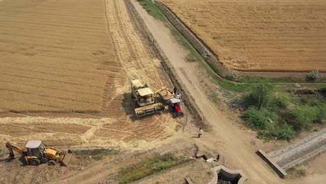 Luftdrohnenaufnahmen-Eines-Mähdreschers,-Der-Von-Einem-Traktor-Unterstützt-Wird-Und-Weizen-Sammelt