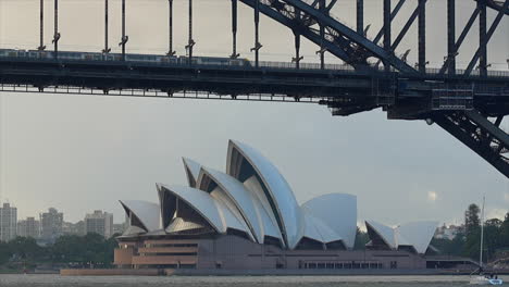 Train-and-boats-pass-by-the-opera-house-in-Sydney,-Australia
