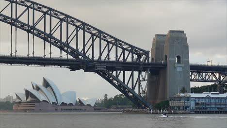 A-small-boat,-ferry-and-train-moving-past-the-bridge-in-Sydney-harbour-Australia