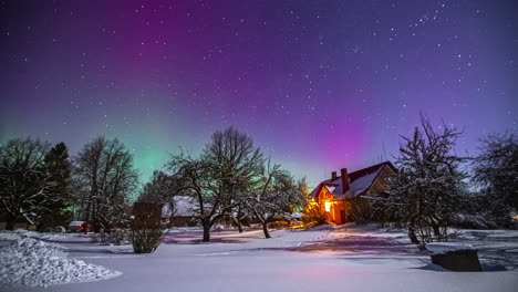 Aurora-borealis-and-milky-way-in-the-sky-over-snowy-landscape-with-trees-and-wooden-house-with-warm-lights