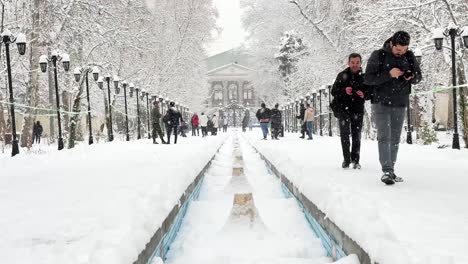 heavy-snow-fall-white-scene-winter-palace-with-white-architecture-design-in-Tehran-old-historical-house-blue-pool-stone-marble-fountain-in-a-row-light-column-trees-a-Persian-Garden-tourist-attraction
