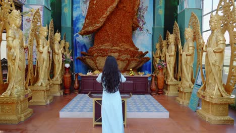 Woman-Worships-A-Giant-Lay-Buddha-Statue-Made-Of-Immortal-Flowers-In-Linh-Phuoc-Pagoda,-Da-Lat-City,-Vietnam