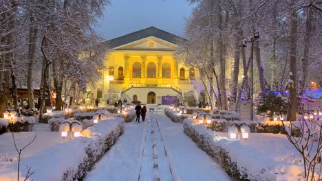 Walking-with-umbrella-in-a-historical-palace-in-Tehran-Iran-in-a-snowy-evening-lots-of-snow-in-city-center-down-town-rare-snowfall-in-Persian-Garden-stone-fountain-spiral-marble-golden-light-design