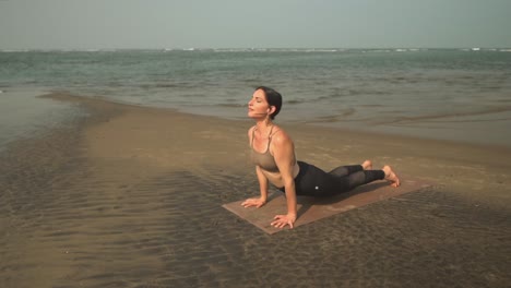 Frau-Macht-Yoga-Übungen-Am-Ufer-Eines-Strandes-Am-Meer