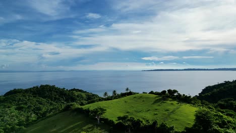 Breathtaking-Aerial-View-of-bird-flying-revealing-stunning-island-hills,-palm-trees,-pristine-ocean-bay-and-cloudscape-of-Catanduanes,-Philippines