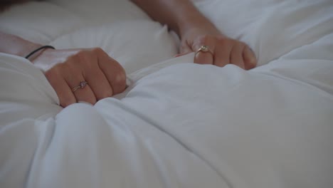 Womans-hands-gripping-white-bed-sheet-tightly