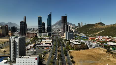 Aerial-view-over-traffic-rising-towards-high-rise-in-sunny-San-Pedro-Garza-Garcia,-Monterrey,-Mexico