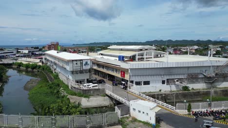 Establecimiento-De-Una-Toma-Con-Drones-Del-Estacionamiento-Ocupado-Y-Un-Pequeño-Río-Junto-Al-Centro-De-La-Ciudad-De-Virac,-Catanduanes