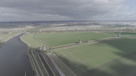 Hohe-Luftdrohnenaufnahme-Einer-Niederländischen-Landschaft-Mit-Windmühlen-Auf-Ackerland-Mit-Fluss