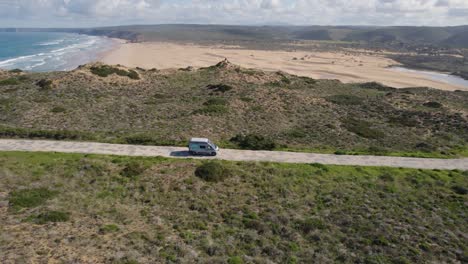 Aerial-view-following-campervan-travelling-coastal-road-along-Portuguese-beachfront-coastline