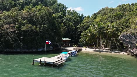 Kleiner-Holzsteg-Mit-Dominikanischer-Flagge-Am-Exotischen-Und-Tropischen-Strand-Der-Bucht-Von-San-Lorenzo,-Nationalpark-Los-Haitises-In-Der-Dominikanischen-Republik