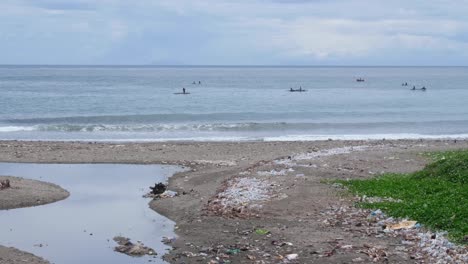 Local-fisherman-in-canoe-boats-checking-on-fishing-nets-along-the-shoreline-with-washed-up-ocean-plastic-pollution-in-capital-city-Dili,-Timor-Leste,-Southeast-Asia
